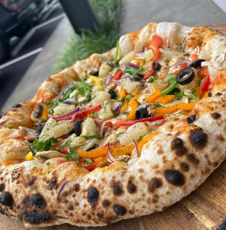 Wood-fired vegetarian pizza with olives, peppers and pineapple on a timber board